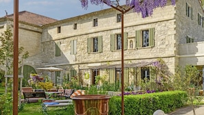 A stone building with green shutters, a garden with a bench, and purple flowers. - Bastide de Bellegarde (Avignon)