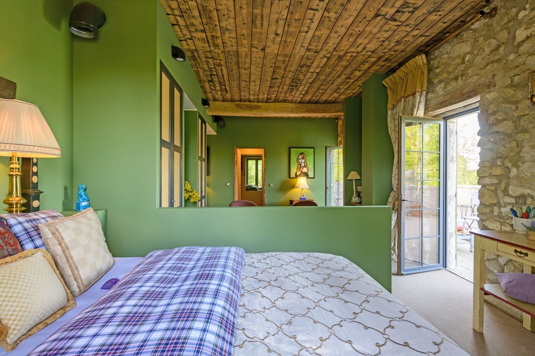 Een slaapkamer met een groot bed, houten plafond, groene wand, stenen wand, een raam en een deur.