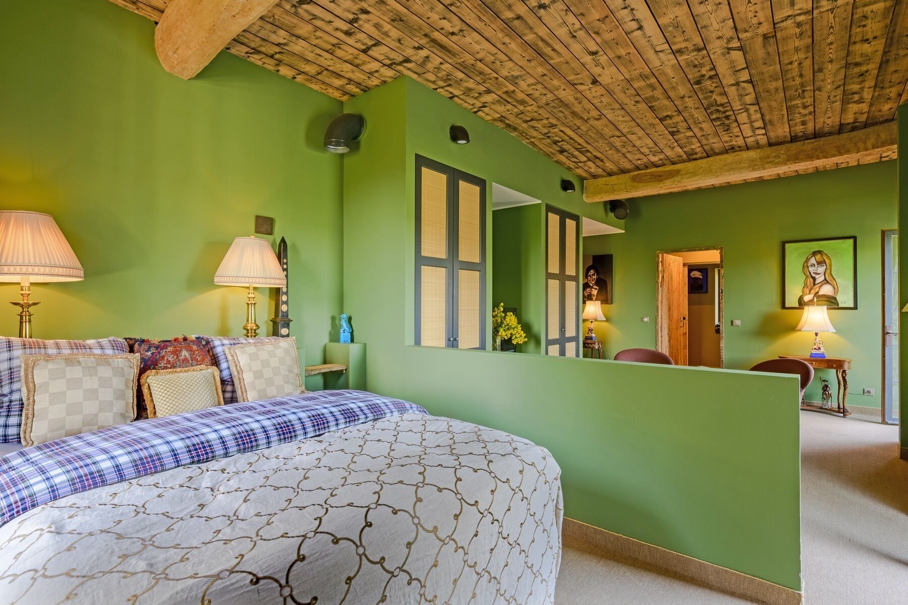 Un dormitorio con una cama, dos lámparas de noche, un tocador, un espejo y una puerta que da a otra habitación.