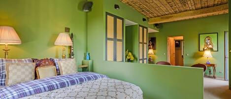 Un dormitorio con una cama, dos lámparas de noche, un tocador, un espejo y una puerta que da a otra habitación.