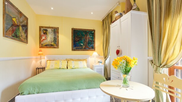 Una camera da letto ordinata con un letto, comodini, un tavolino rotondo con un vaso di fiori e una sedia.