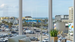 A view from a window overlooking a busy street with buildings and a beach in the background. - Boardwalk Pent House | Ocean Views + Beach Access! (Carolina Beach)
