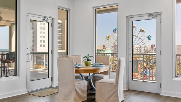 A dining area with a round table, four chairs, and a potted plant. - Boardwalk Pent House | Ocean Views + Beach Access! (Carolina Beach)