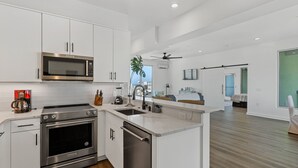 A modern kitchen with stainless steel appliances, a dishwasher, and a large island. - Boardwalk Pent House | Ocean Views + Beach Access! (Carolina Beach)