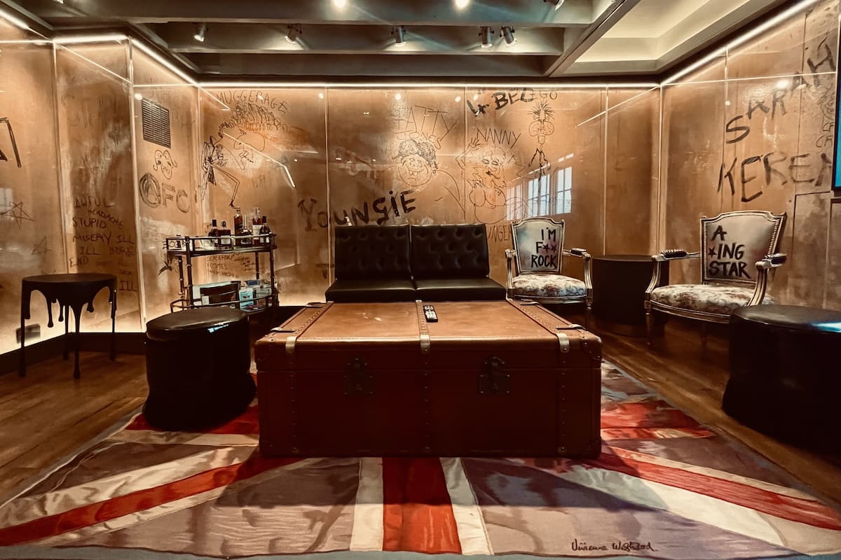 A room with a large bed, a chest of drawers, and a small table. The walls are decorated with graffiti and drawings.