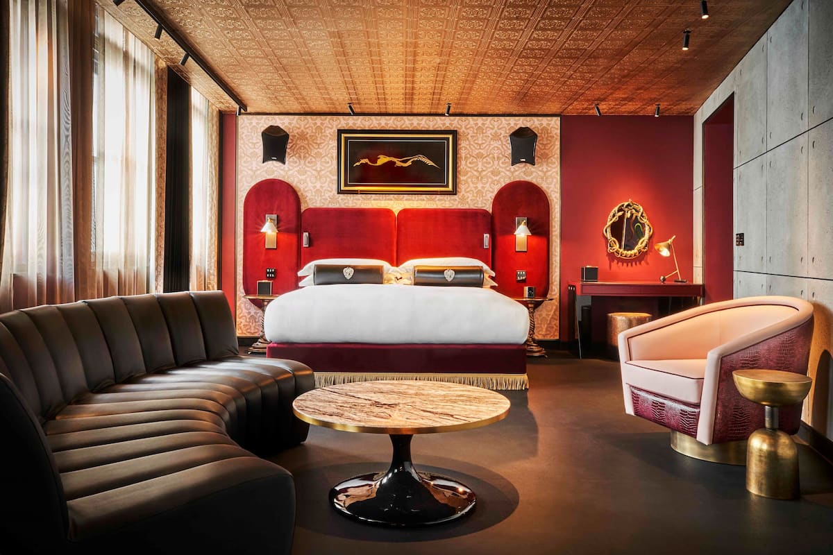 A modern hotel room with a large bed, a sofa, a round coffee table, and a small side table.