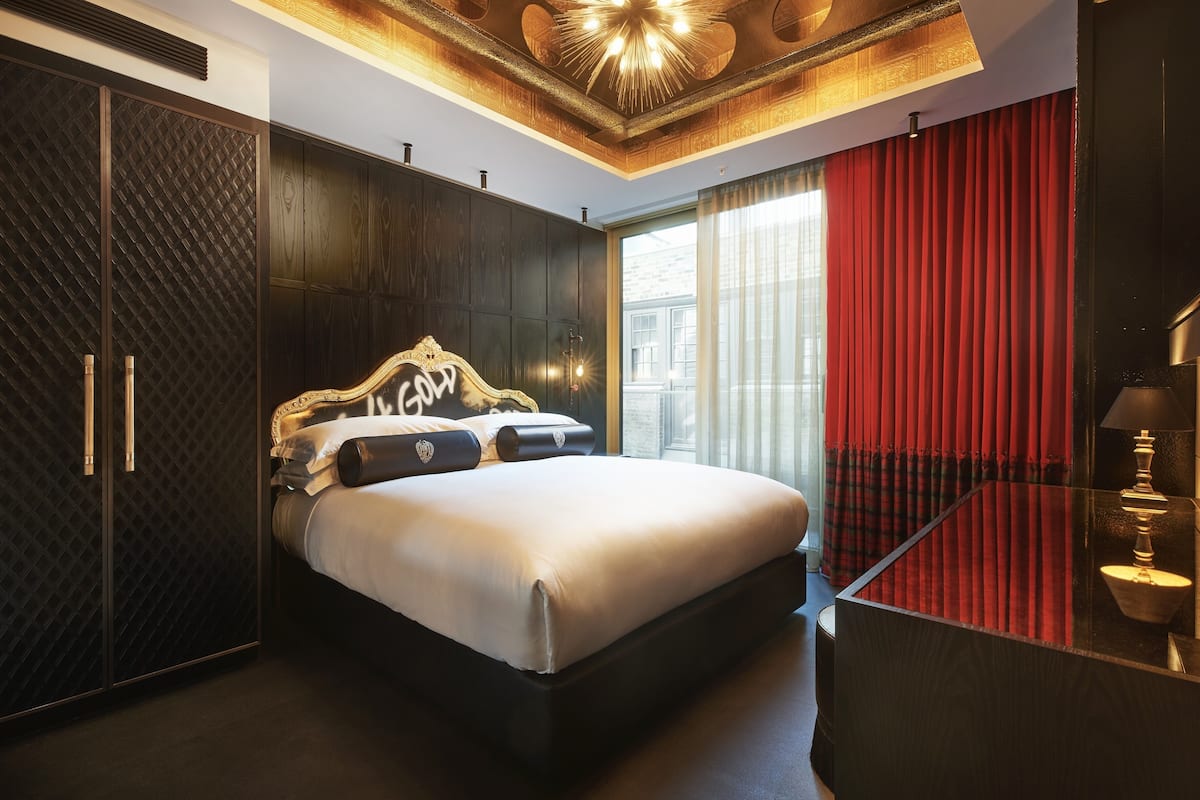 A modern bedroom with a large bed, dark wood paneling, a red curtain, and a unique ceiling design.