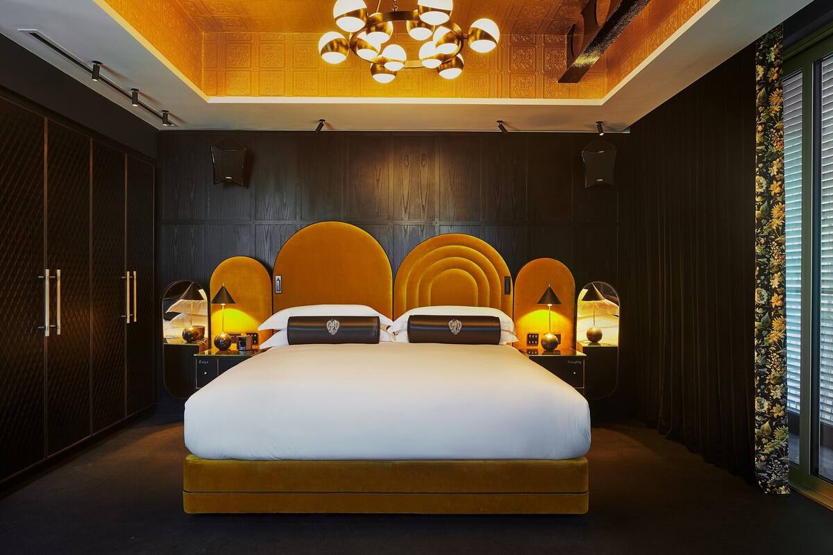 A modern bedroom with a large bed, wooden paneling, and a unique ceiling design.