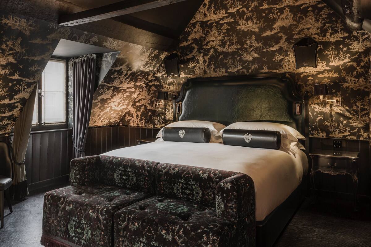 A bedroom with a large bed, a bench, and a window with curtains.