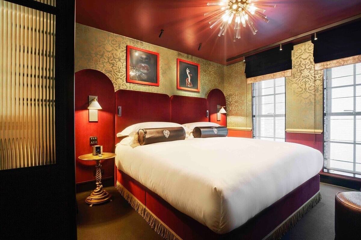 A large bed with a red headboard, two wall-mounted lamps, and framed artwork on the wall.