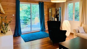 A wooden-paneled room with a large sliding glass door to a garden, a black chair, a white sofa, and a table. - House not available (Tarnos)