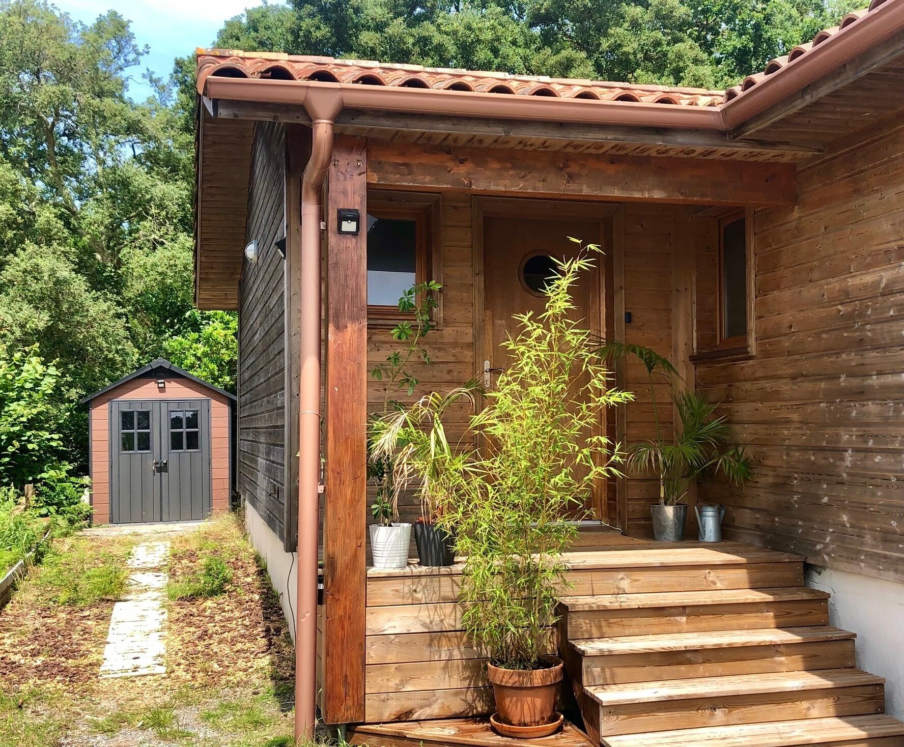 Une maison en bois avec un porche, un petit abri de jardin et un escalier menant à l’entrée.