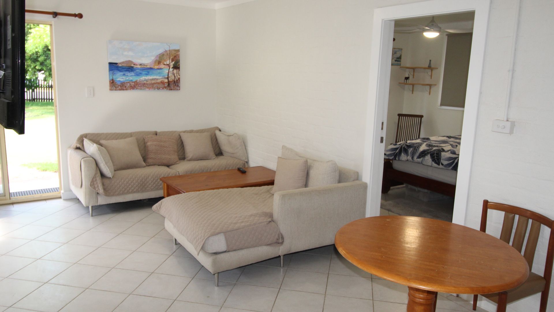 A living room with a sofa, a coffee table, and a bed with a patterned bedspread.