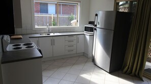 A kitchen with white cabinets, a stainless steel refrigerator, a microwave, and a window with a view of a fence and greenery.