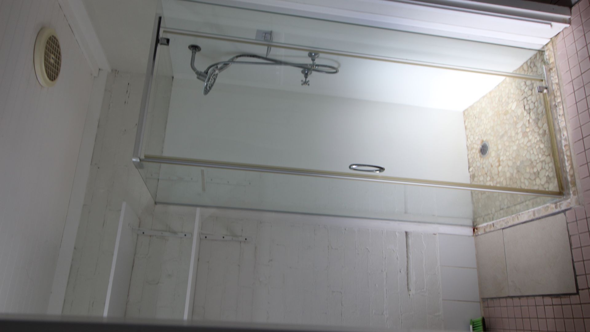 A shower with a glass door, a handheld showerhead, and a wall-mounted faucet.