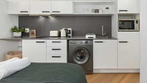 A modern kitchen with white cabinets, a washing machine, a microwave, and a toaster. - Bridgewater One Studio Apartment | DSTV | Fibre (Cape Town)