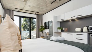 A modern hotel room with a large bed, a kitchenette, a dining area, and a balcony with a view of trees. - Bridgewater One Studio Apartment | DSTV | Fibre (Cape Town)