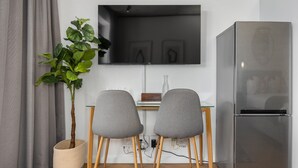 A modern kitchen with a built-in refrigerator, two grey chairs, a small table, and a potted plant. - Bridgewater One Studio Apartment | DSTV | Fibre (Cape Town)
