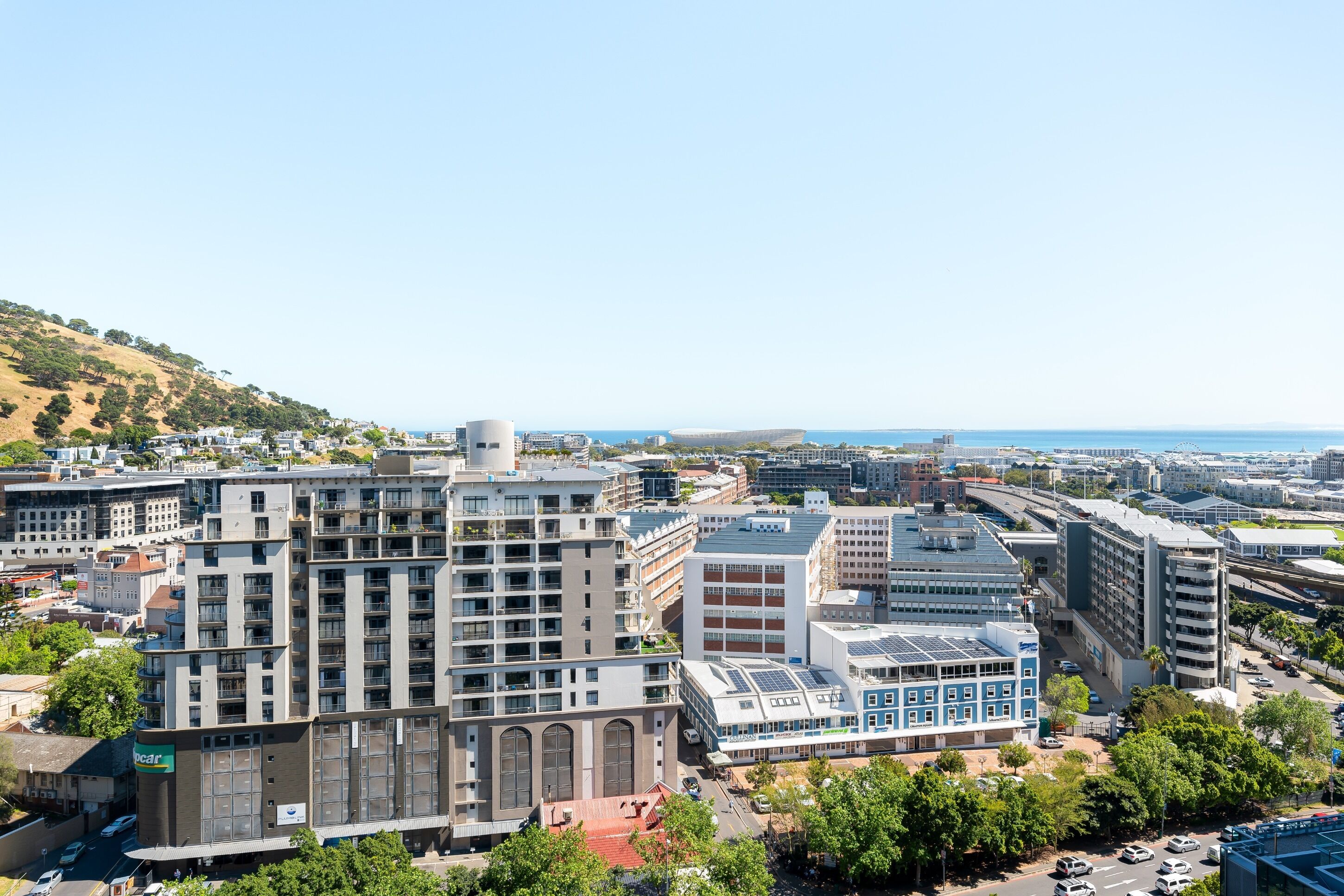 A multi-story hotel with a central courtyard, surrounded by other buildings, and a view of the sea.