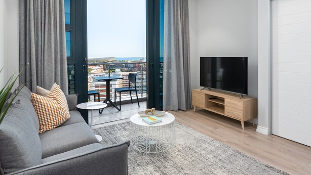 A modern living room with a sofa, coffee table, and TV stand. - Lush Sky Apartment With Ocean Views (Cape Town)
