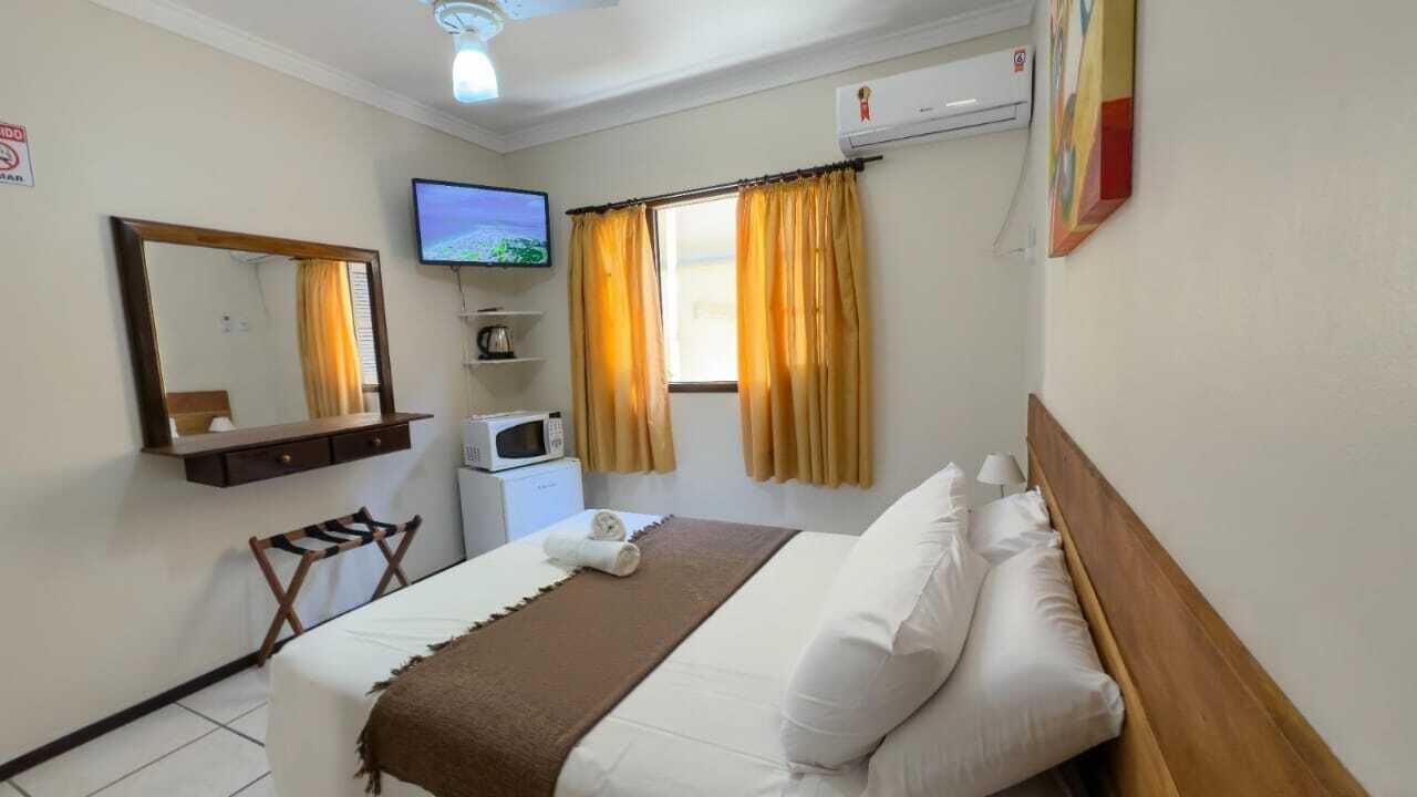 Habitación de hotel con cama, televisión, microondas, escritorio, silla y ventana con cortinas.