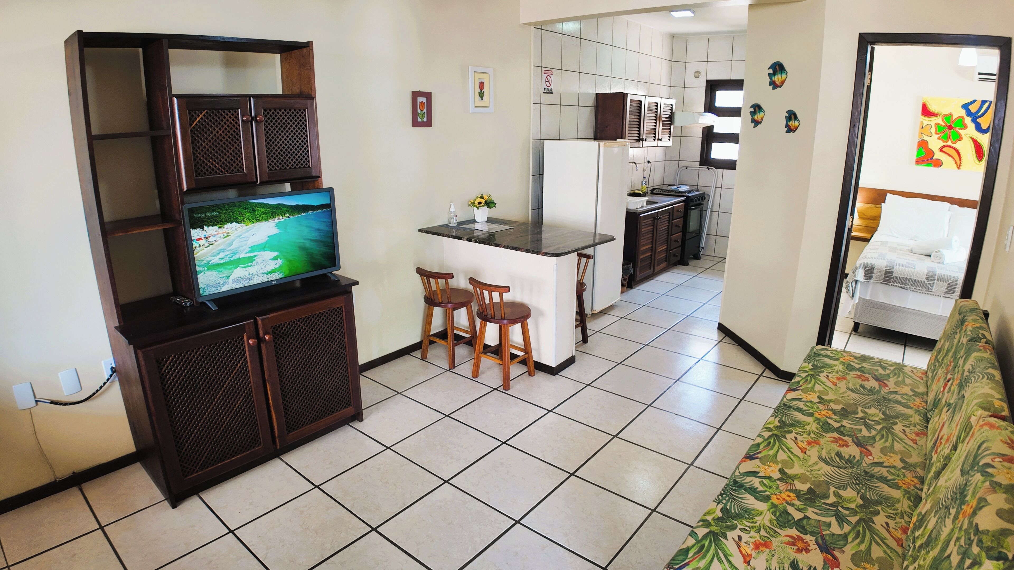 A compact living space with a TV on a wooden stand, a kitchenette, a sofa, and a small dining area.