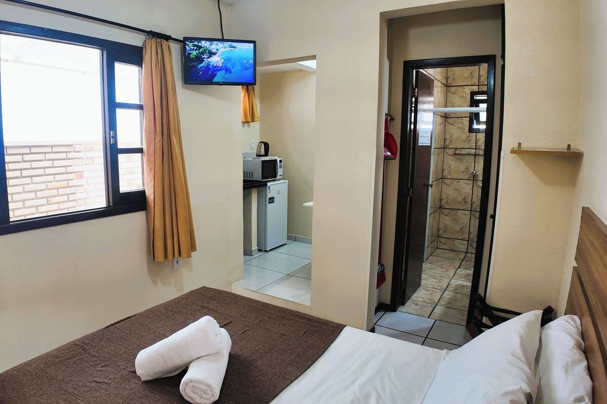 Une chambre d’hôtel avec un lit, un téléviseur fixé au mur, une fenêtre avec des rideaux et une vue sur l’extérieur.