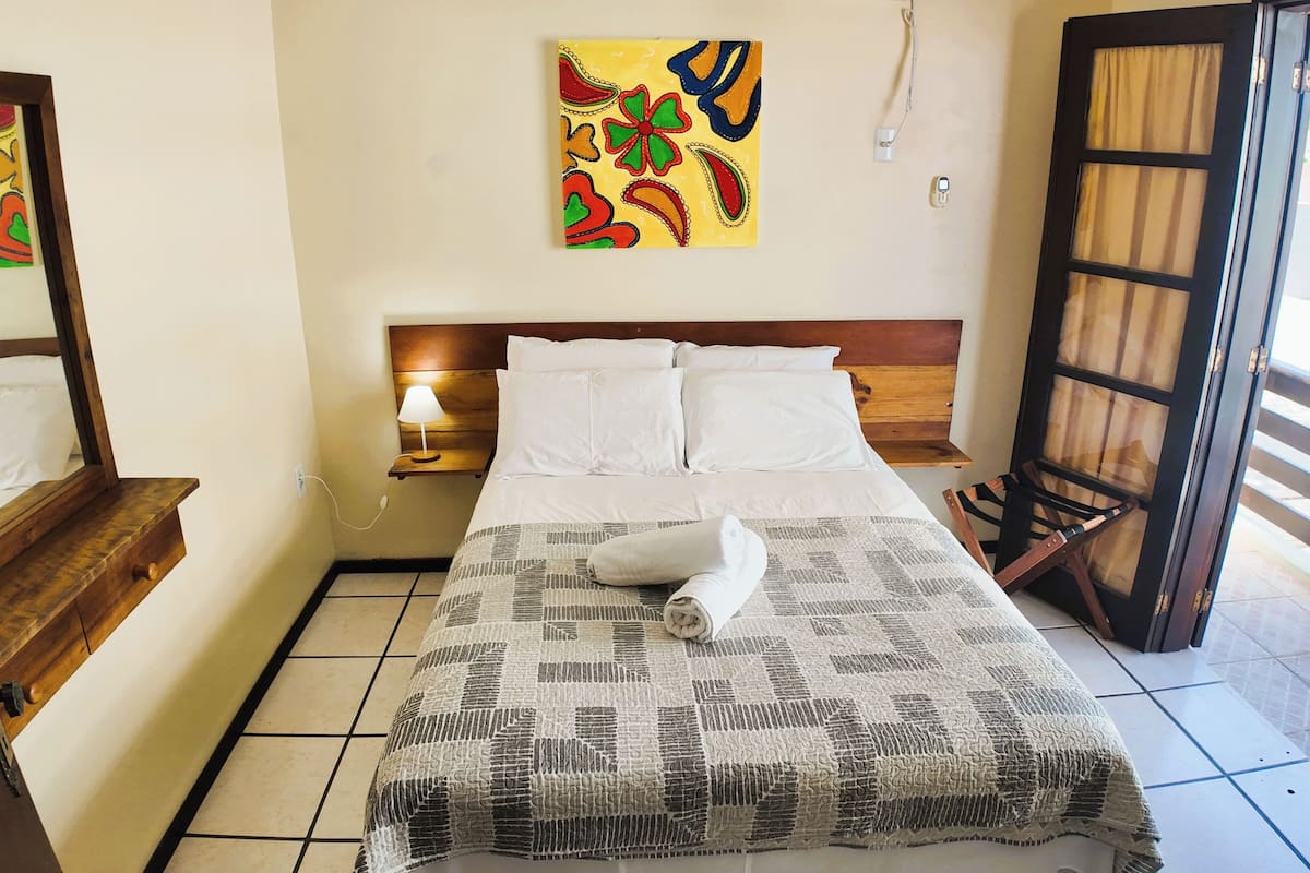 Une chambre d’hôtel avec un lit, une table de chevet, une lampe, une fenêtre avec des rideaux et un tableau au mur.