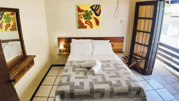 A hotel room with a bed, a nightstand, a lamp, a window with curtains, and a painting on the wall.