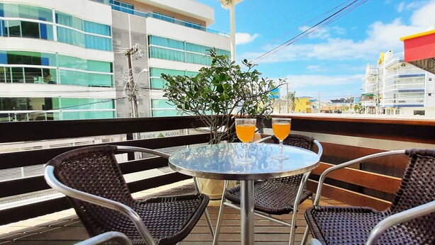A balcony with wicker chairs and a round table, a potted plant, and two glasses of orange juice. - Agua Marinha de Bombas - Bombinhas (Bombinhas)