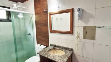 A bathroom with a glass shower enclosure, a wooden vanity with a granite countertop, a white toilet, and a wall-mounted hairdryer.