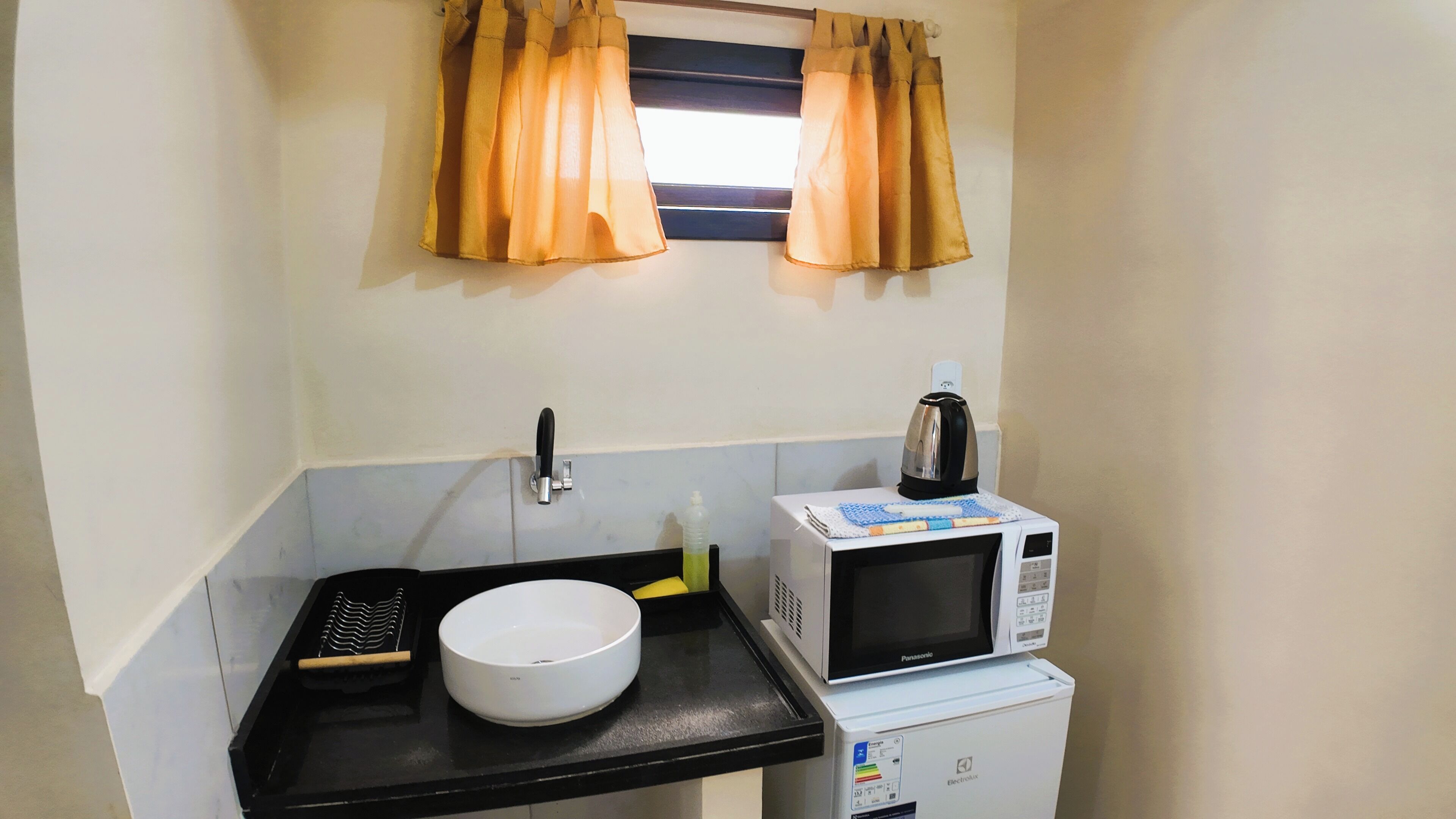 A compact kitchenette with a white bowl, a kettle, a microwave, and a sink.