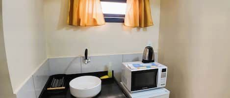 A compact kitchenette with a white bowl, a kettle, a microwave, and a sink.