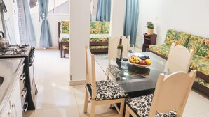 A dining area with a glass table, chairs, a sofa, and a kitchen with a stove. - Agua Marinha de Bombas - Bombinhas (Bombinhas)