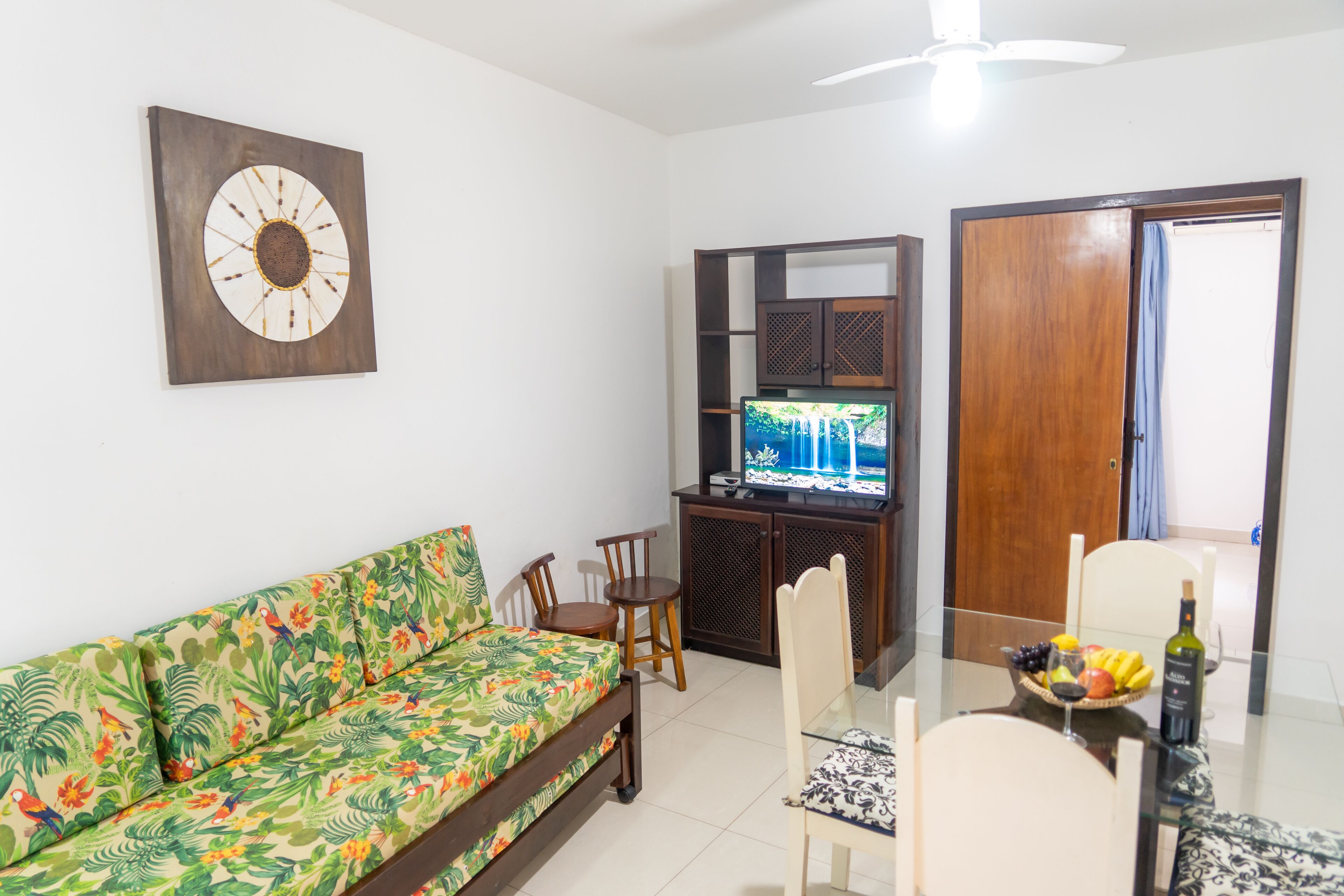 A living room with a sofa, a TV, a dining table with chairs, and a wooden cabinet.