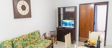 A living room with a sofa, a TV, a dining table with chairs, and a wooden cabinet.