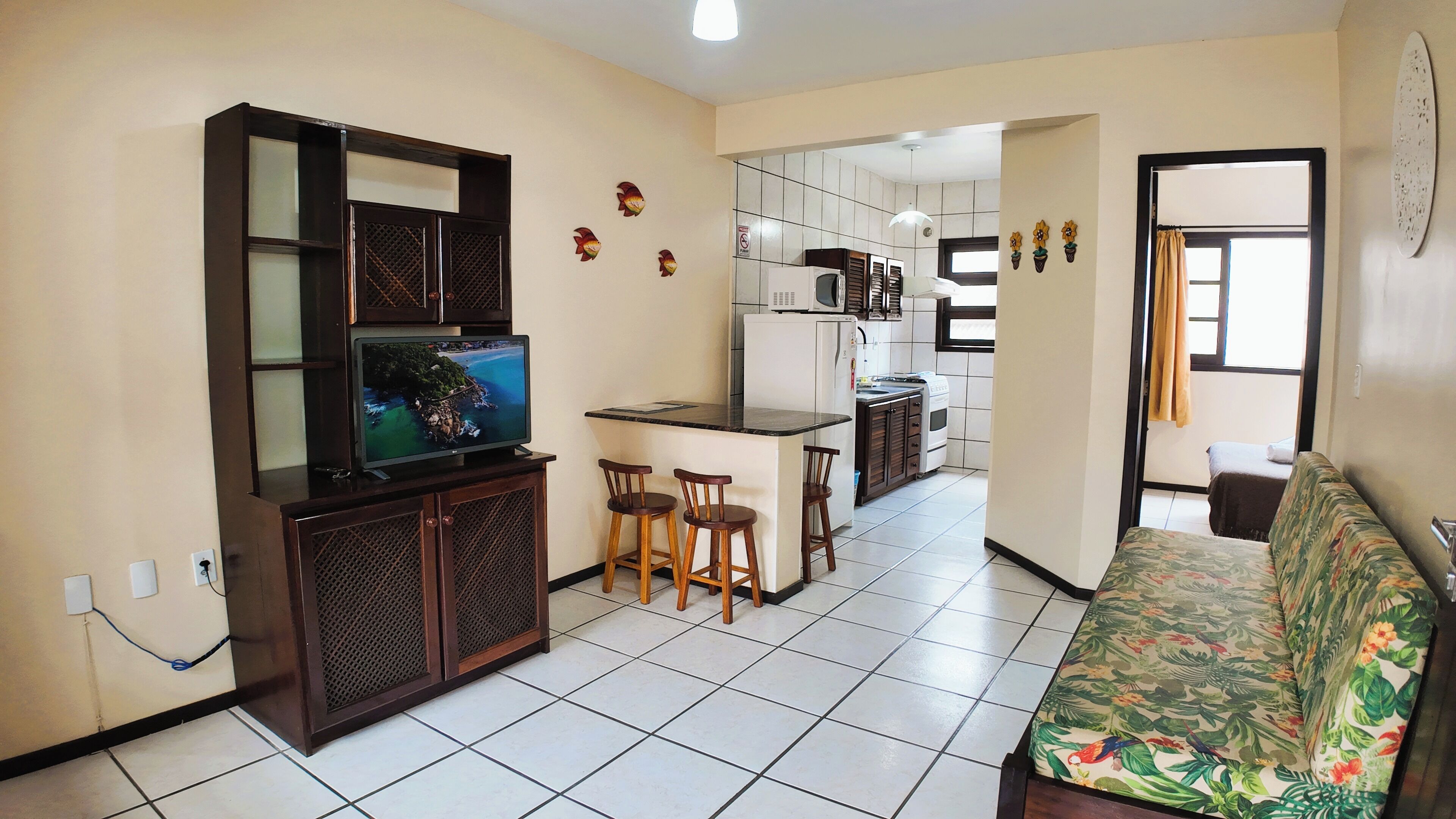 A compact living space with a kitchenette, a television on a cabinet, a sofa, and a small dining area with stools.