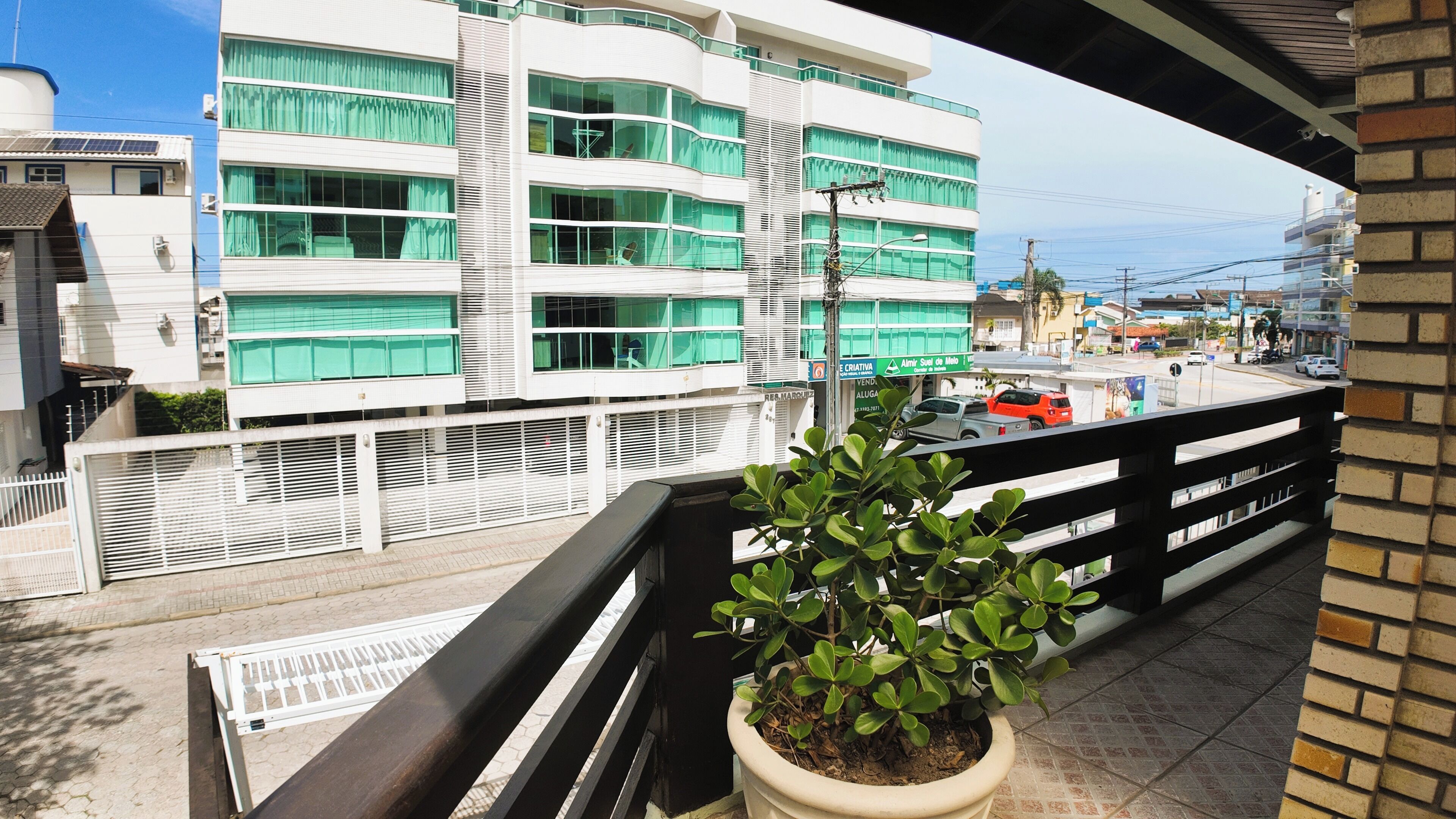 A balcony with a potted plant, overlooking a street with buildings and parked cars.