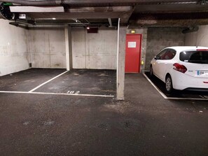 A parking garage with concrete walls, a red door, and a white car parked in a space marked 102.
