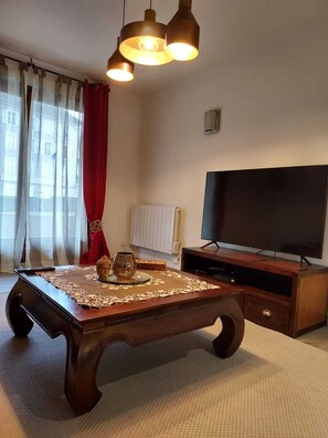 Una sala de estar con una mesa de centro de madera, un televisor de pantalla plana y una cortina roja.