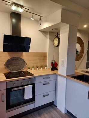 Una cocina moderna con horno empotrado, microondas, estufa y lavabo. Hay un reloj en la pared y una pequeña planta en la encimera.