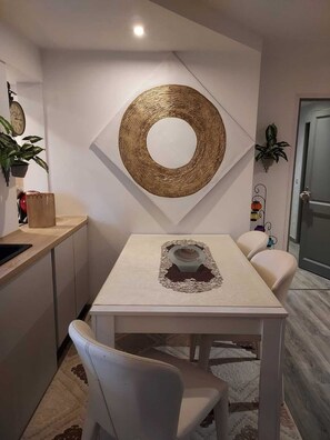 A modern kitchen with a white table, two chairs, a decorative mirror, and a clock on the wall.