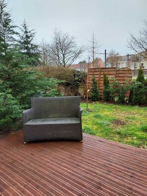 A grey outdoor sofa on a wooden deck with a grassy area and trees in the background.