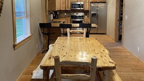Un intérieur rustique avec une table à manger en bois, un coin cuisine doté d’appareils électroménagers en acier inoxydable et une grande fenêtre.