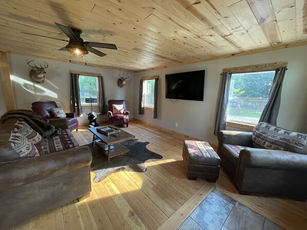 A cozy living room with wooden flooring, a ceiling fan, a mounted TV, and a deer head on the wall. - Fully Remodeled Story Cabin minutes from mountain trails! (Story)