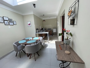 A dining area with a round table, four chairs, and a kitchen in the background.