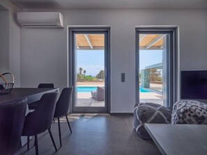 Un salon moderne avec vue sur la piscine, un coin repas et un canapé agrémenté de coussins à motifs.