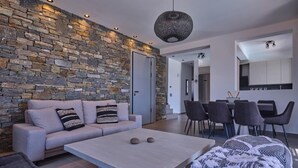 En moderne stue med en stenvæg, en sofa, et sofabord og et spiseområde med stole.