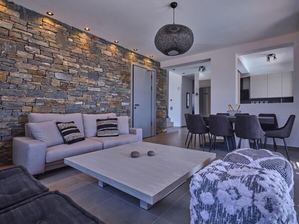 Un salon moderne avec un mur en pierre, un canapé, une table basse et un coin repas avec des chaises.
