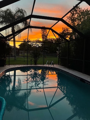 Ein Swimmingpool mit Blick auf einen Sonnenuntergang durch eine Glasfassade.